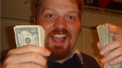 jason holding stacks of money in each hand with a bleep eating grin on his face