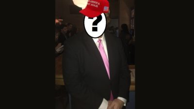 man in a suit with his face obscured by a question mark and a maga hat photoshopped onto his head
