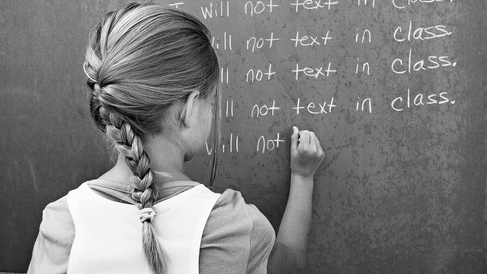 stock photo of a girl writing i will not text in class n a chalkboard