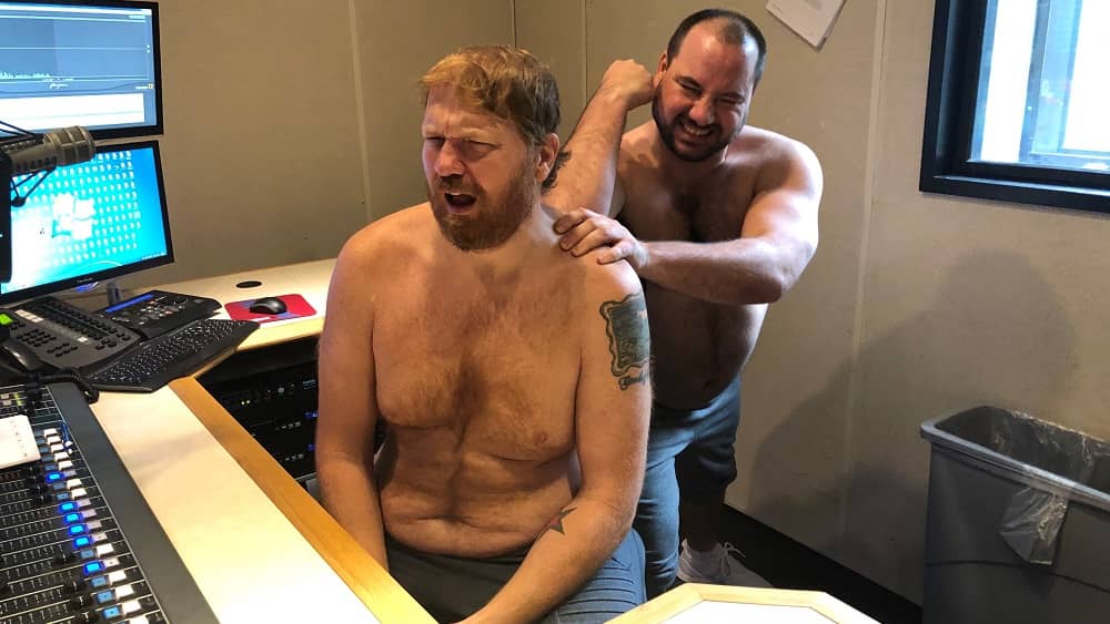 a shirtless nick giving a shirtless jason a back massage in the studio