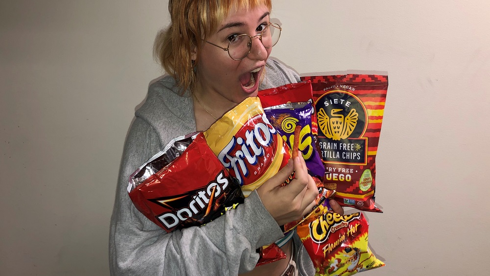 emily holding a bunch of bags of various brands of hot chips