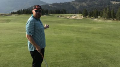 Jason in Montana golfing and pointing to mountains