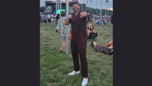dave b posing in front of acl flags wearing brown ups style onesie
