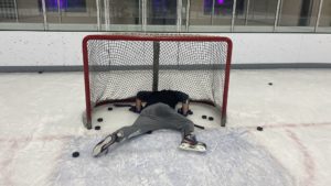 nick layin on the ice in the goalie net