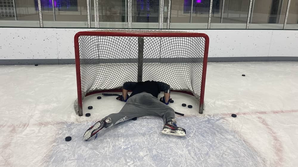 nick layin on the ice in the goalie net