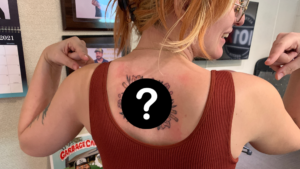 Emily Pointing at her new tattoo on her back with a question mark over it