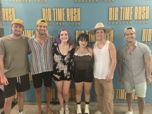 Emily's two friends standing next to the members of Big Time Rush