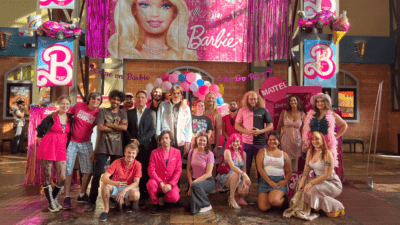 Emily and a big group of friends posing after the Barbie movie in front of Barbie decorations in the theater while wearing pink