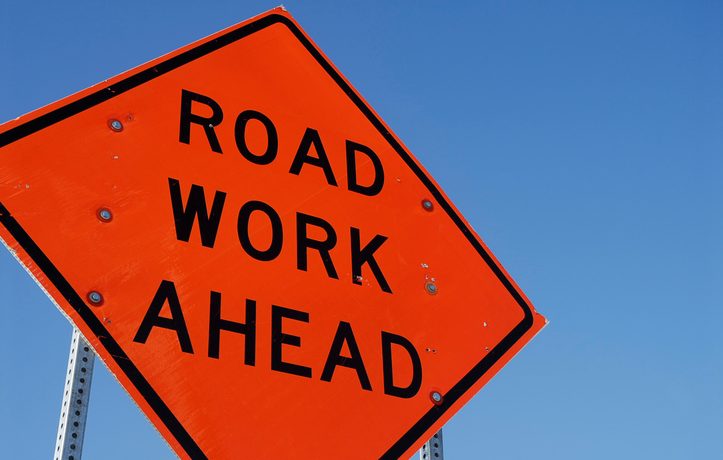 An orange diamond-shaped road sign: "Road Work Ahead"