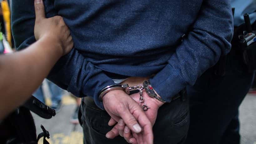 A man escorted away from a crime scene in handcuffs. Photo by Anthony Wallace/Getty.