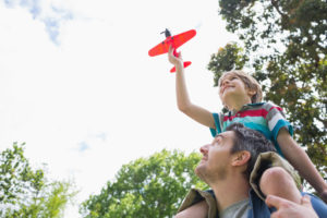 Boy with toy airplane sitting on father's shoulders