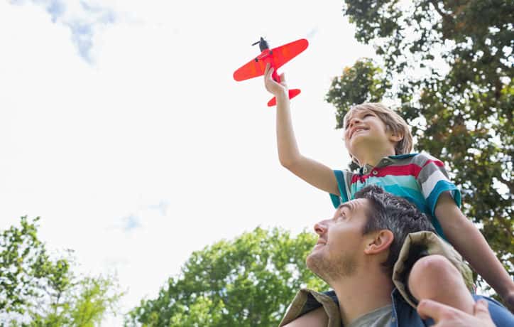 Boy with toy airplane sitting on father's shoulders