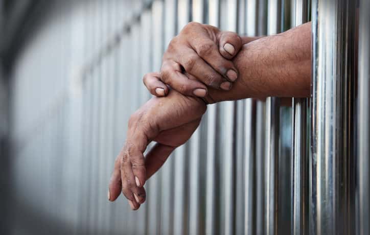 Person with hands out from jail bars