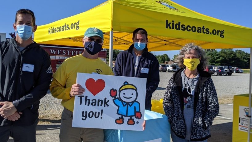 Four volunteers witha 'thank you' sign in front of a Kids Coats Tent and donation station.