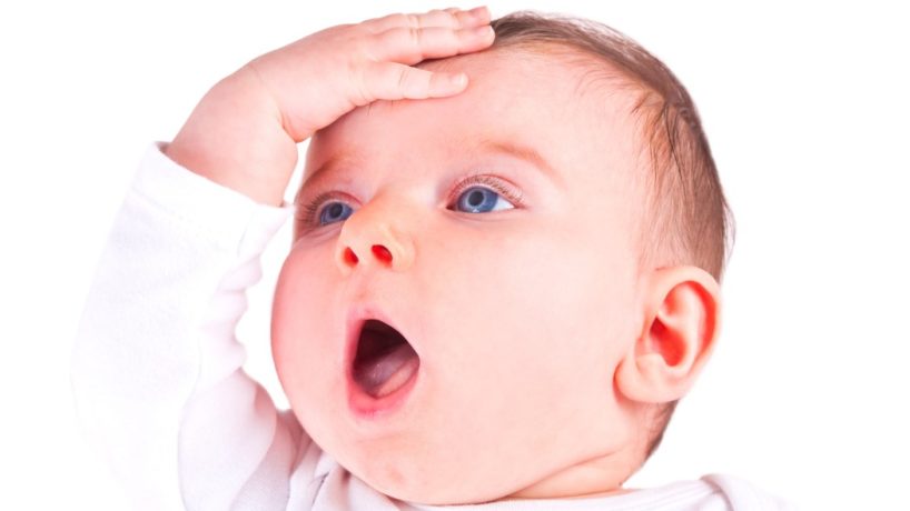 An infant with bright blue eyes smacks his forehead in disbelief.