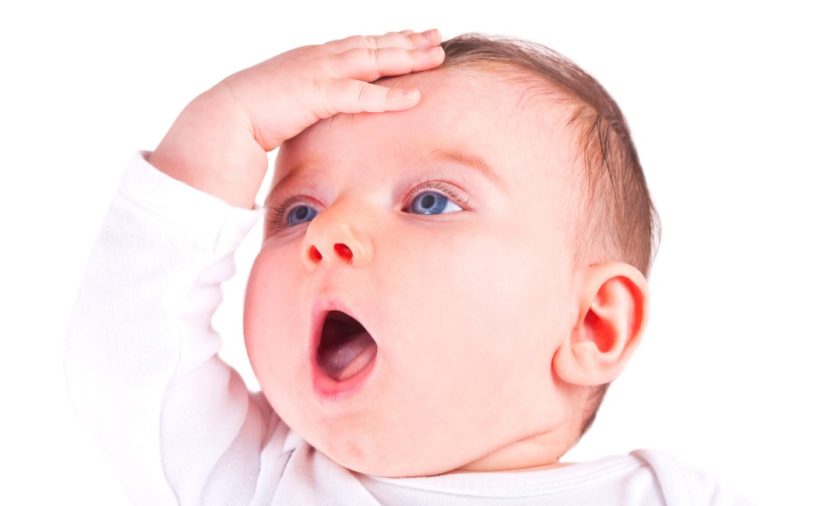An infant with bright blue eyes smacks his forehead in disbelief.