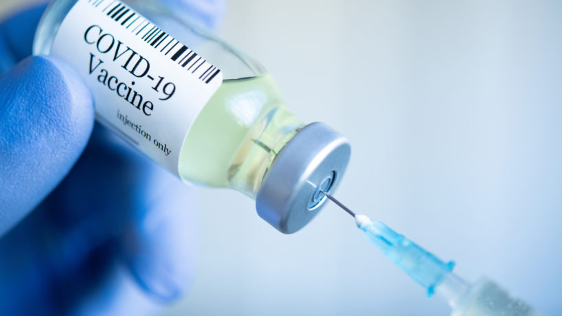 Doctor drawing up Covid-19 vaccine from glass phial bottle and filling syringe injection for vaccination.