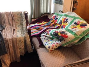 Knitted and homemade dresses and blankets folded over a couch
