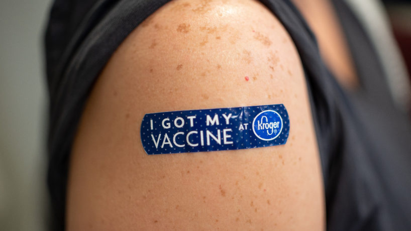 A person with a blue Band Aid reading "I Got My Vaccine at Kroger".