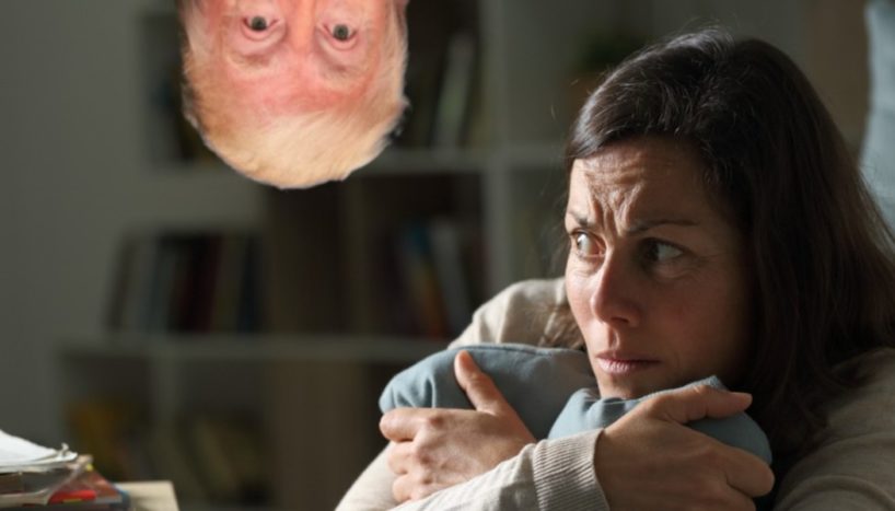 Donald Trump appears upside down, looking at a middle aged woman who is clutching her arms in fear.