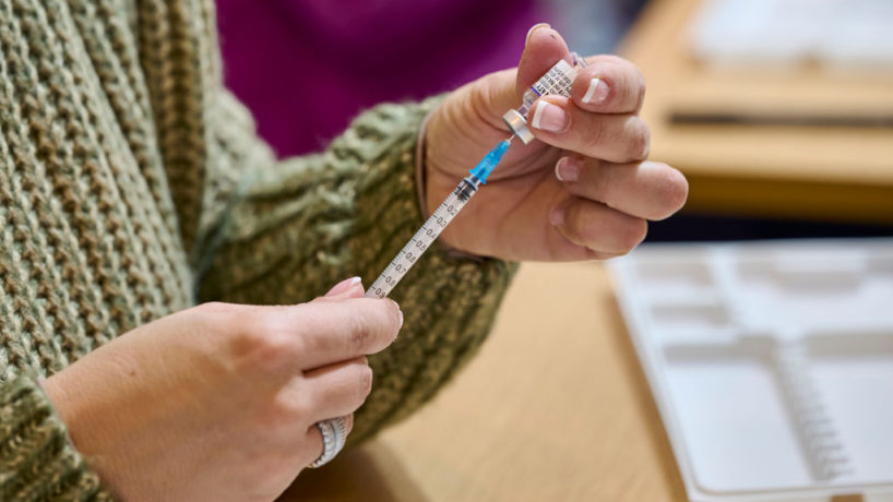 A mask-clad health technician prepares doses of Pfizer-BioNTech COVID-19 vaccine.