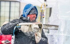 A professional ice carver sculpting a block of ice with a chainsaw.