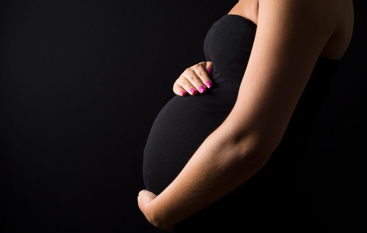 Side view of a pregnant woman body with her hands on her tummy on black background.