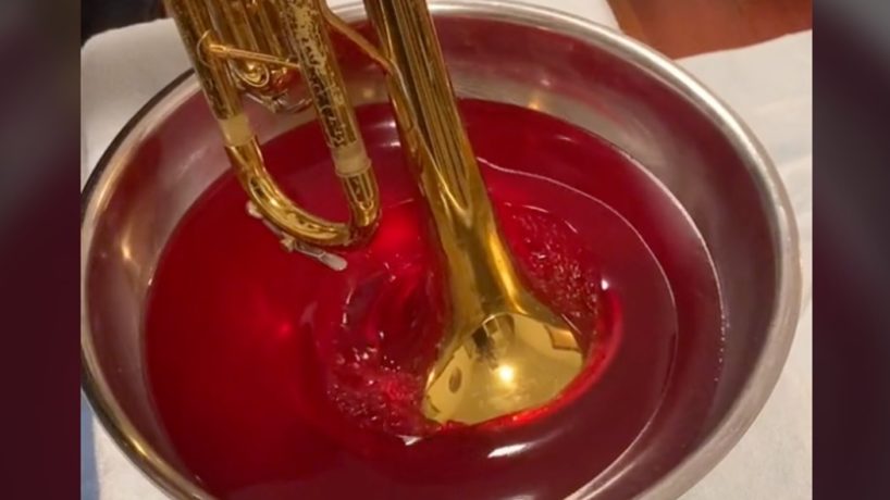 A screen capture shows a man blowing a trumpet into a tub of Jell-O.