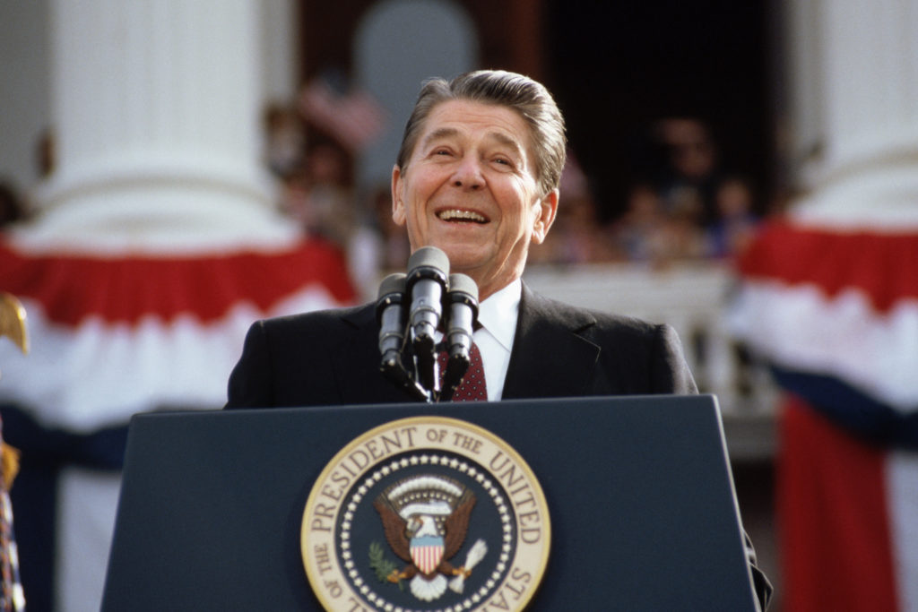 Former president Ronald Reagn smiling behind a podium