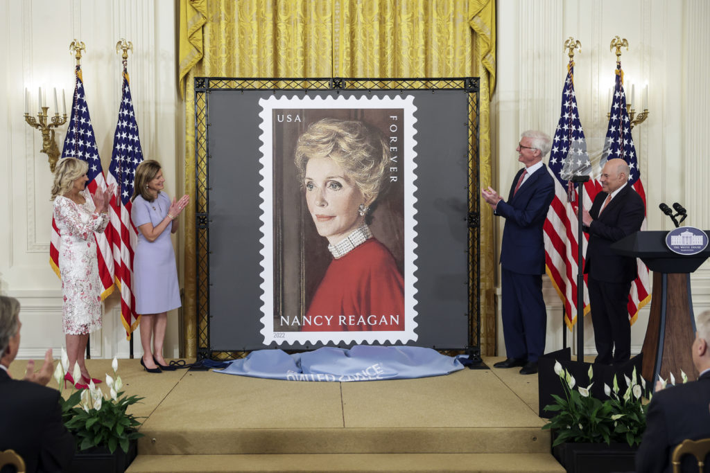 First Lady Jill Biden, Anne Peterson, Nancy Reagan’s niece, Fred Ryan, Chairman of the Board of Trustees of The Ronald Reagan Presidential Foundation and Institute and Louis DeJoy, U.S. Postal Service Postmaster General, unveil the Nancy Reagan stamp, in the East Room at the White House 