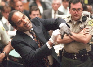 Double murder defendant O.J. Simpson puts on one of the bloody gloves as a Los Angeles Sheriff's Deputy looks on during the O.J. Simpson murder trial 15 June. One of the gloves was found at the murder scene, while the other was found at Simpson's state. AFP PHOTO (Photo credit should read SAM MIRCOVICH/AFP via Getty Images)