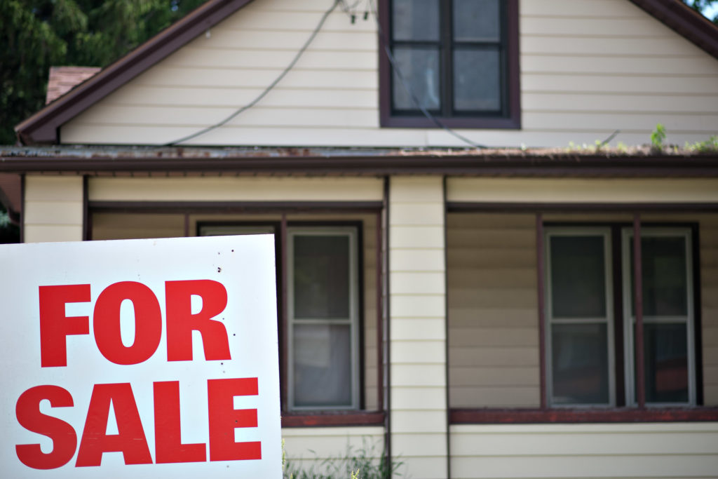 A "for sale" sign stands outside a home