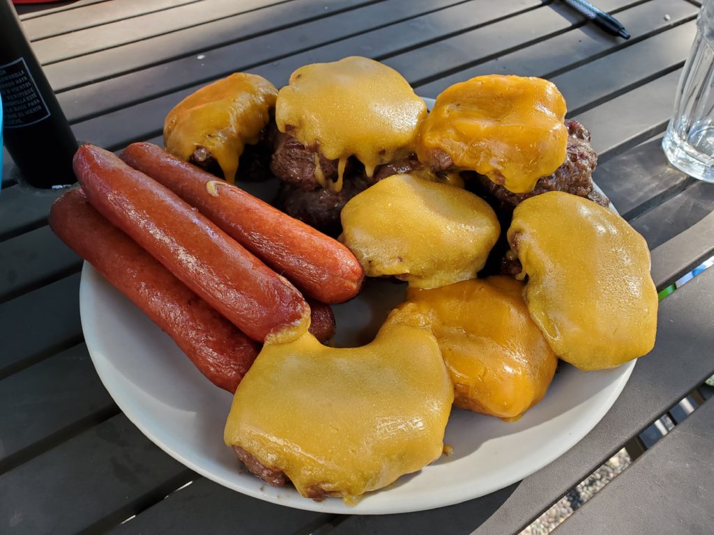 Homemade cheeseburgers and hot dogs are visible during a cookout