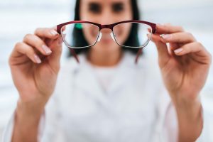 Cropped image of attractive young female doctor in ophthalmology clinic. Doctor ophthalmologist is standing near shelves with di
