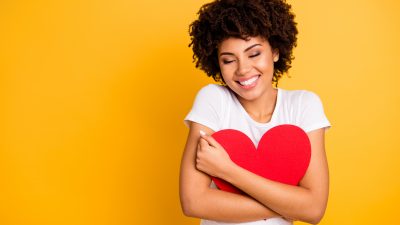 Attractive woman with curly brown hair in a white shirt cuddling big paper card heart shape figure
