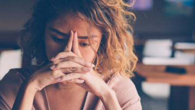 Closeup of sad young Asian woman at cafe leaning head on clasped hands and staring into vacancy