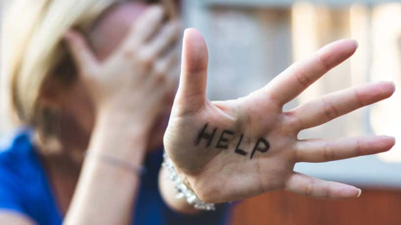 Woman gesturing "help" sign on her hand.