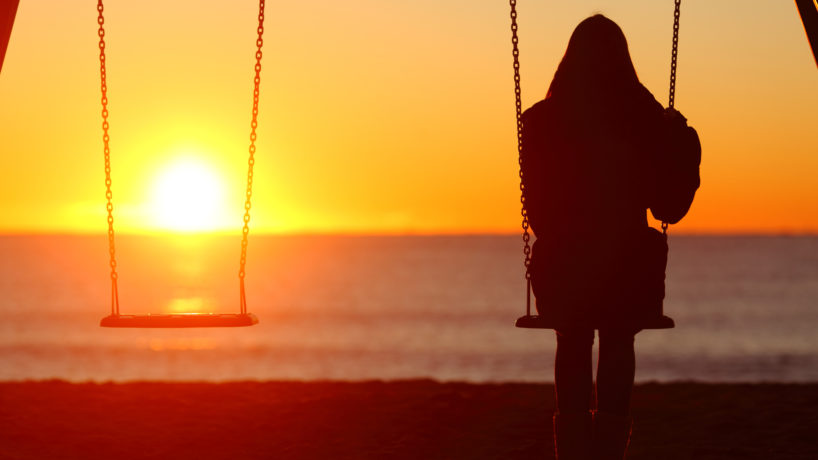 Single woman sitting on a swing contemplating sunset