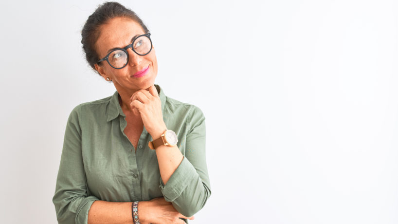 Middle age woman wearing green shirt and glasses standing over isolated white background with hand on chin thinking about question, pensive expression. Smiling with thoughtful face. Doubt concept. - stock photo