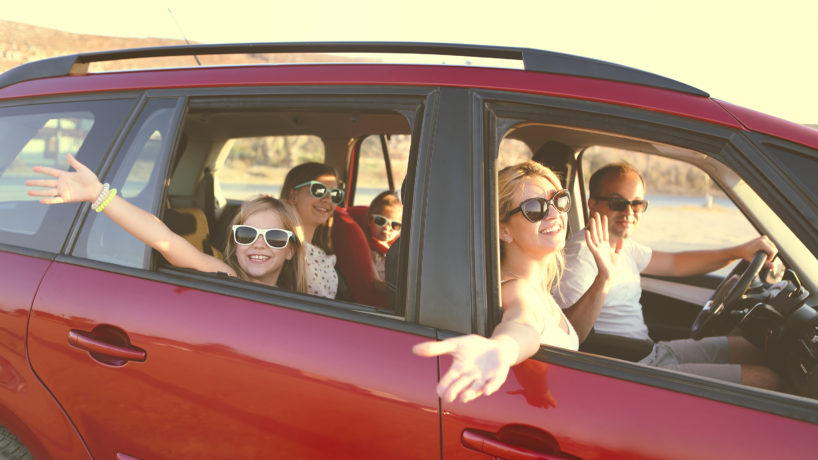 Happy smiling family with daughters in the car with sea background. Portrait of a smiling family with children at beach in the car. Holiday and travel concept