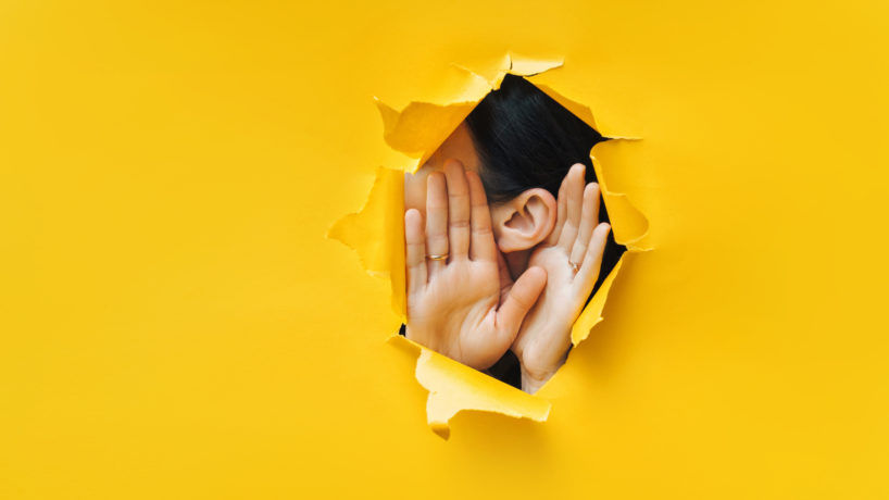 Female ear and hands close-up. Copy space. Torn paper, yellow background. The concept of eavesdropping, espionage, gossip and the yellow press.