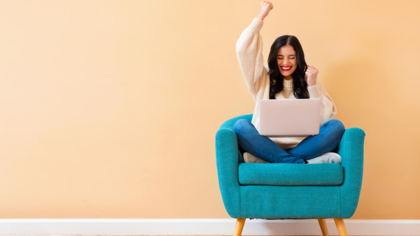 Young woman with a laptop computer with successful pose sitting in a chair