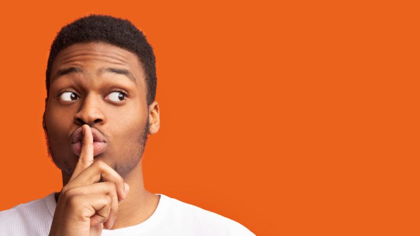 Shh, It's A Secret. Black man making silence gesture putting finger on his lips looking at copy space, panorama