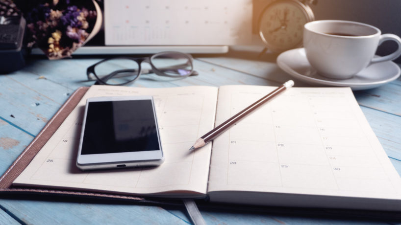 Diary Calendar and agenda for Planner to plan timetable,appointment,organization at office. Desktop Calender 2020,smartphone,clock,book and cup of coffee place on desk,work from home.Calendar Background Concept