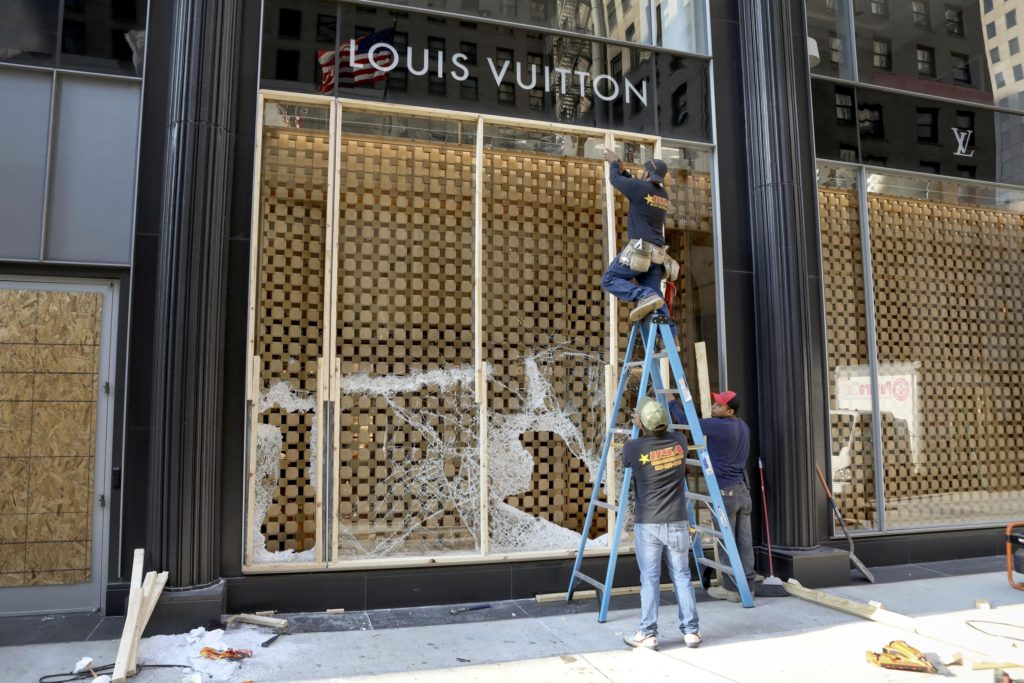 FILE - Workers begin to board up a display window at the Louis Vuitton store Monday, Aug. 10, 2020, after overnight vandals hit many high-end stores in Chicago. The Illinois Senate has a bipartisan plan to crack down on a recent spate of smash-and-grab retail thefts and the fencing that follows. Bill sponsor Western Springs Democratic Sen. Suzy Glowiak Hilton says smash-and-grab crimes not only result in product loss but terrorize employees and patrons and damage property. (AP Photo/Teresa Crawford, File)
