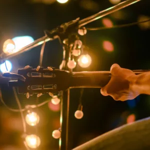 Rear view of the man sitting play acoustic guitar on the outdoor concert with a microphone stand in the front