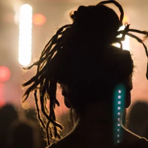 Close up portrait of an anonymous performer/ silhouette with dreadlocks^ back to camera^ watching a concert on stage with music^ retro light effect^ flashlight and spotlight in a festival.