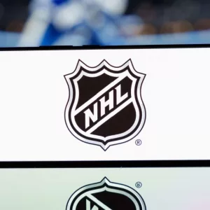 A smartphone displaying the NHL logo with a blurred hockey game in the background. January 13^ 2025