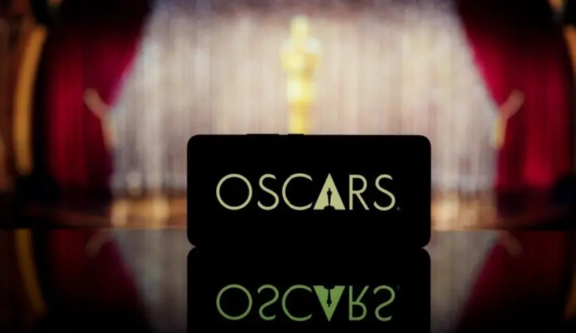 A smartphone displaying the Oscars logo against a blurred awards ceremony background. January 13^ 2025
