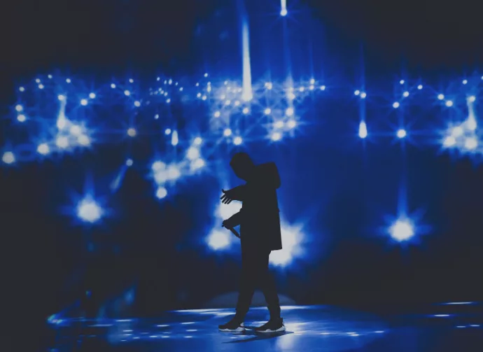 Rap/ hip hop star / singer perform on stage of nightclub in front of bright screen with stars.